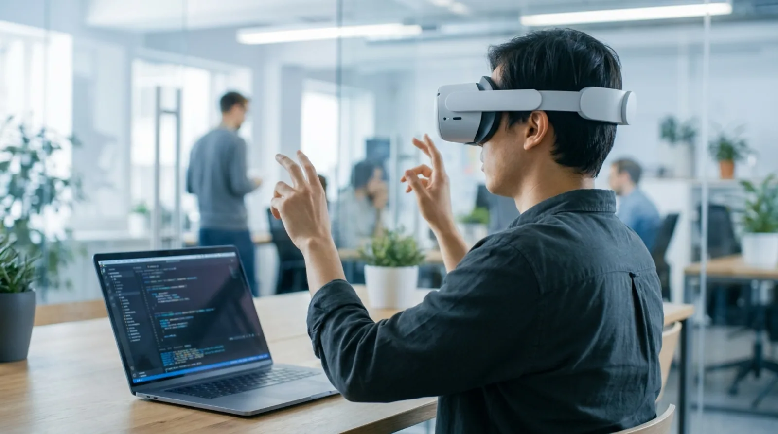 Person wearing a modern mixed reality headset in an office with a laptop showing a development environment
